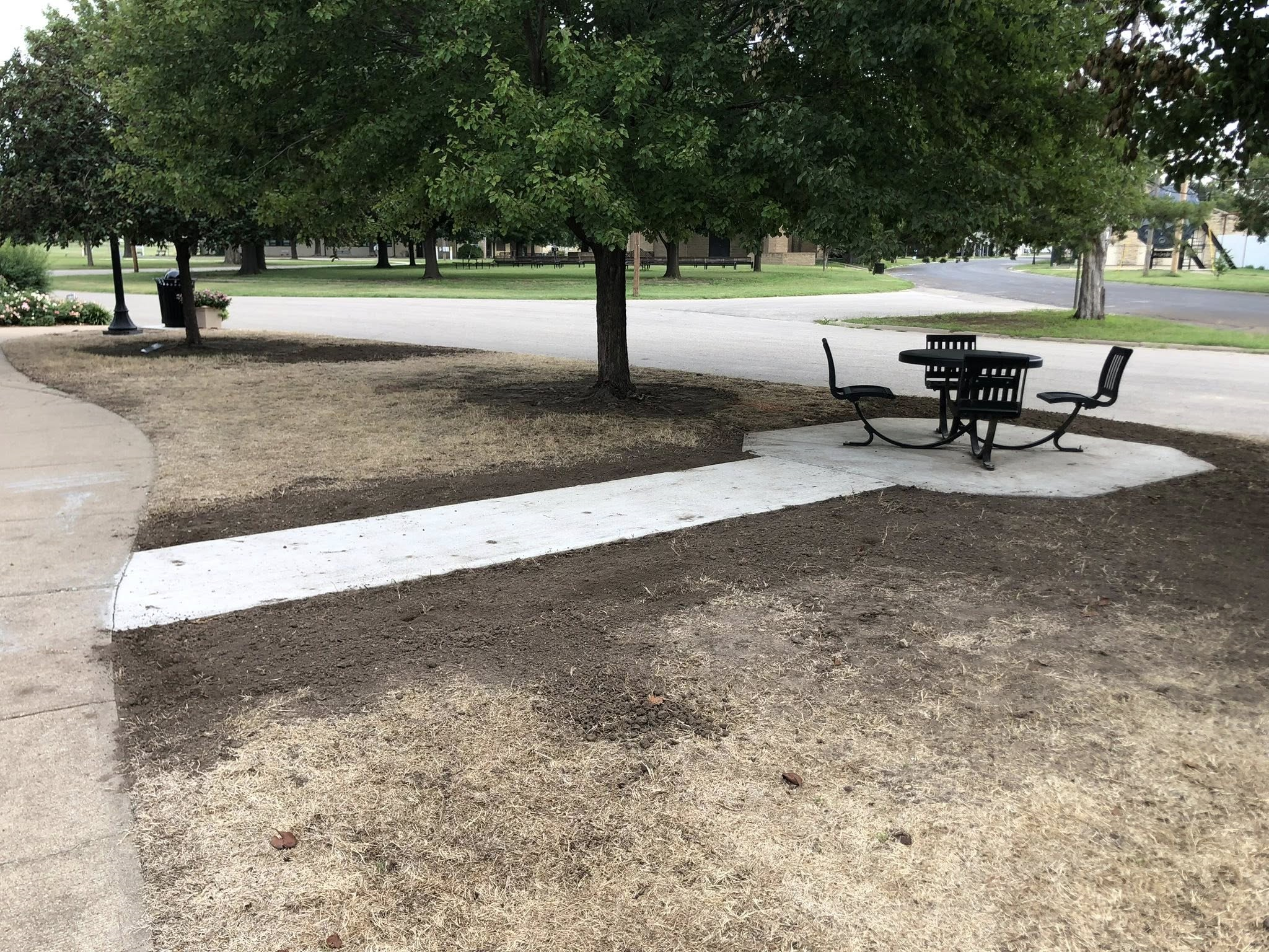 New sidewalk leading to shaded picnic table in park.