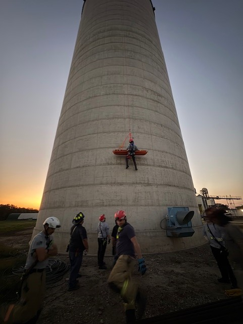 Firefighter suspended on ropes during high-angle rescue training on a concrete tower.