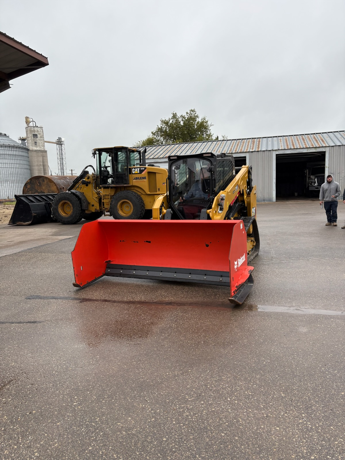 City staff operating snow equipment, including a skid steer with a large red snow pusher attachment.
